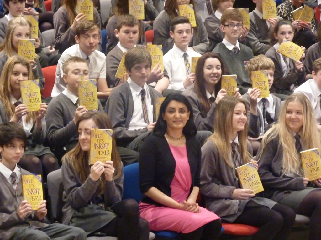 Aneeta Prem seated among pupils holding the gold edition of But It's Not Fair