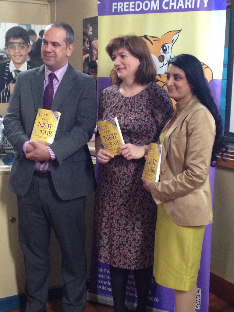 Three adults presenting the gold edition of But It's Not Fair beside a Freedom Charity display